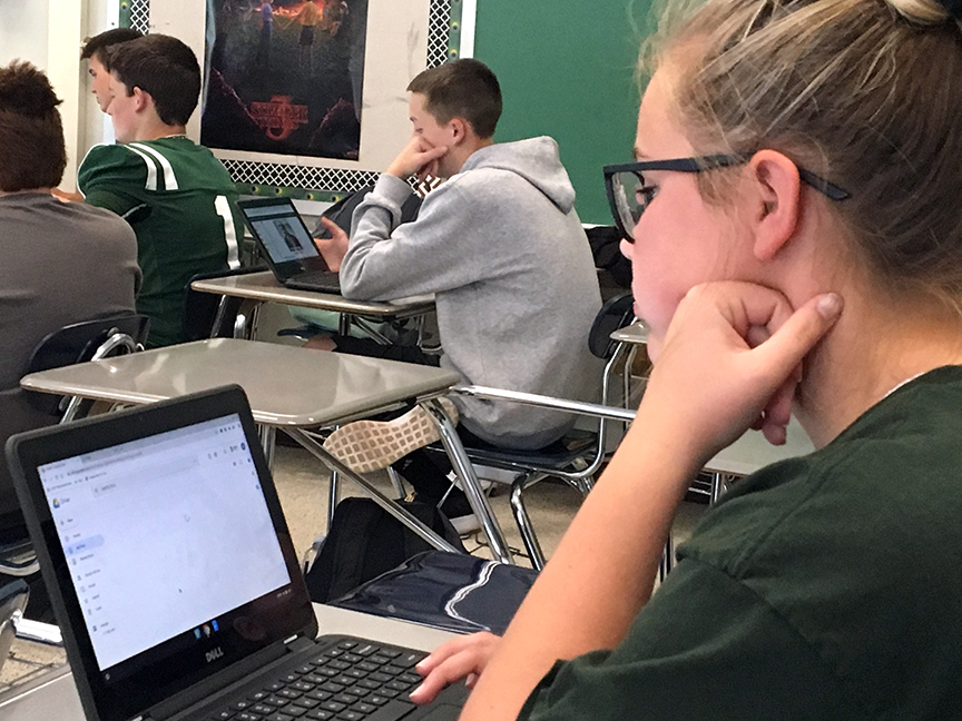 a student in a classroom sits at her desk and looks at her computer