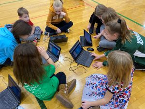 Elementary students work on computers on the gym floor