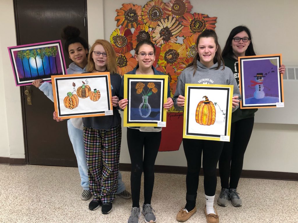 Student artists hold their artwork in front of the camera. 