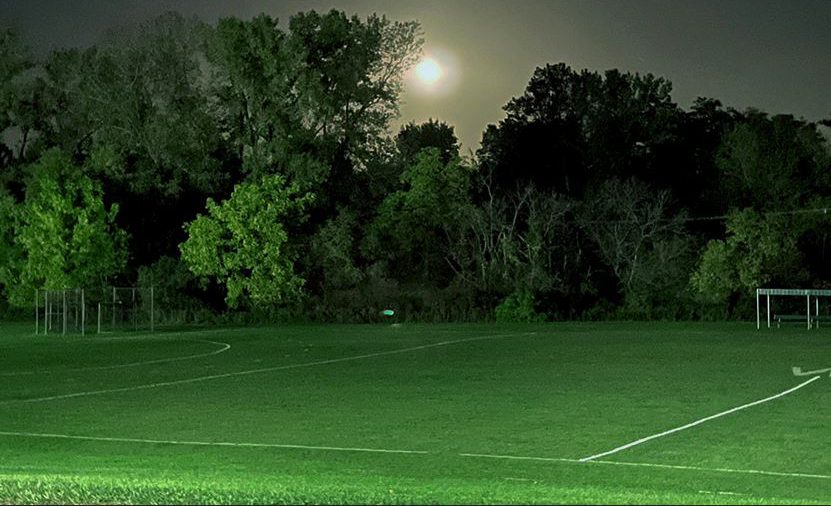 The moon rises over the field hockey practice field at night