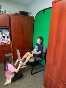 Third grade students perform reports in front of a green screen for metamorphosis project.